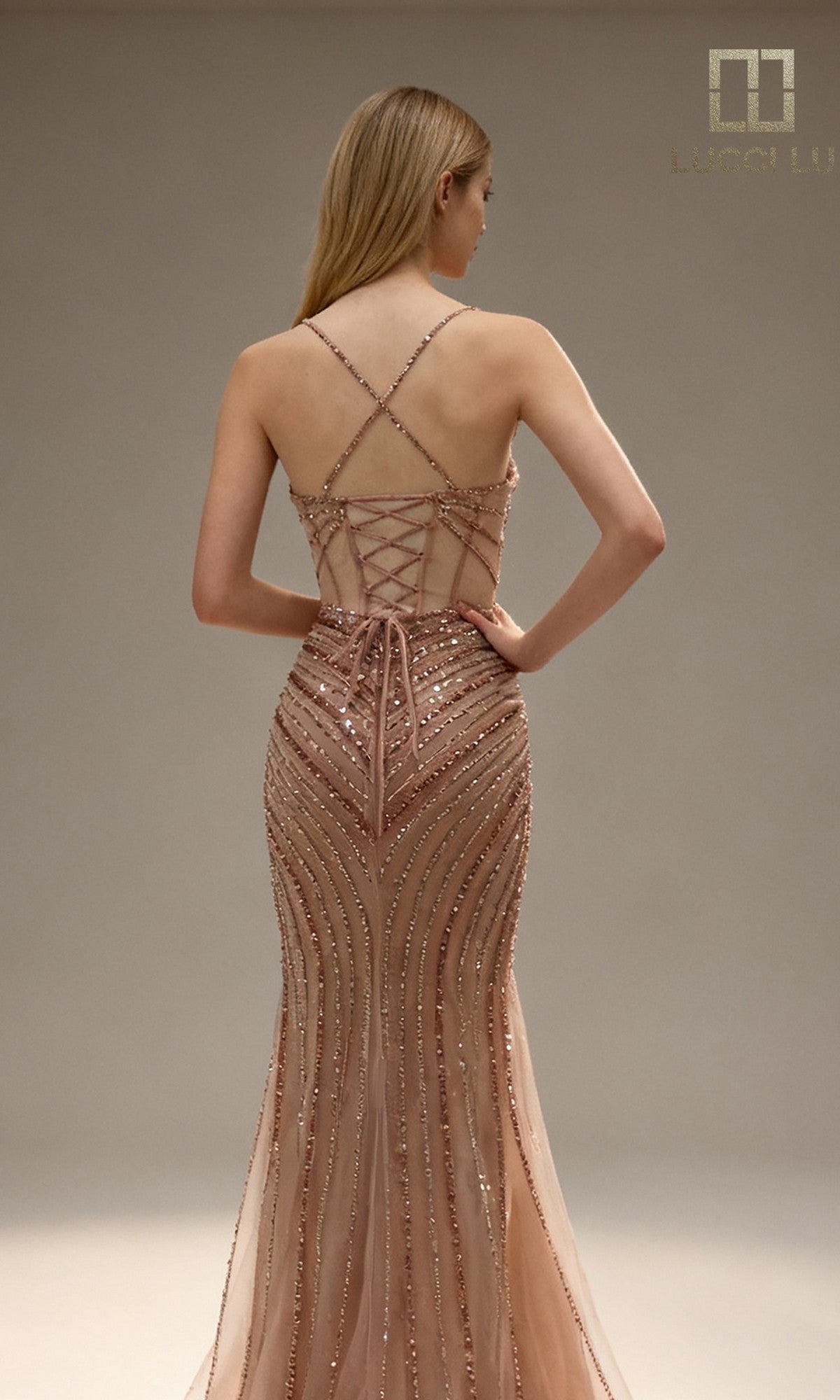 A woman faces away, wearing the Lucci Lu 1448 long prom dress in rose gold, featuring sequins, criss-cross straps, beaded details, and a lace-up back.